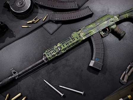 Green camouflaged assault rifle with curved magazine on a table.