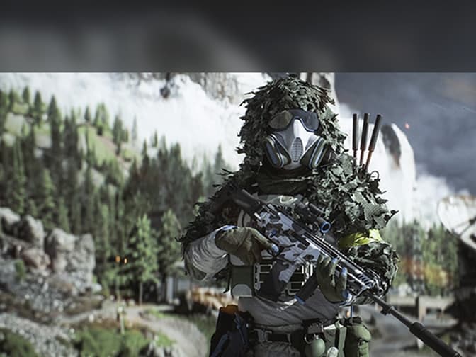 Camouflaged soldier in a gas mask holding a rifle in a mountainous battlefield with trees and smoke.