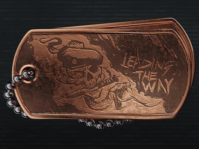 A bronze dog tag etched with a skull in a beret, a snake, and the words "Leading The Way."