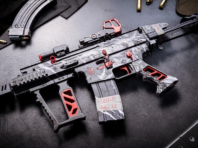 A combat assault rifle with camo skin and orange details.