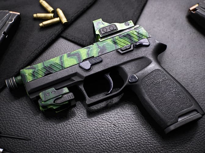 Compact pistol with green camouflage slide and mounted sight.