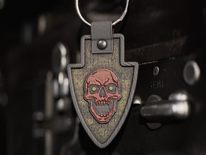 Shield-shaped weapon charm with embroidered red skull, yellow eyes